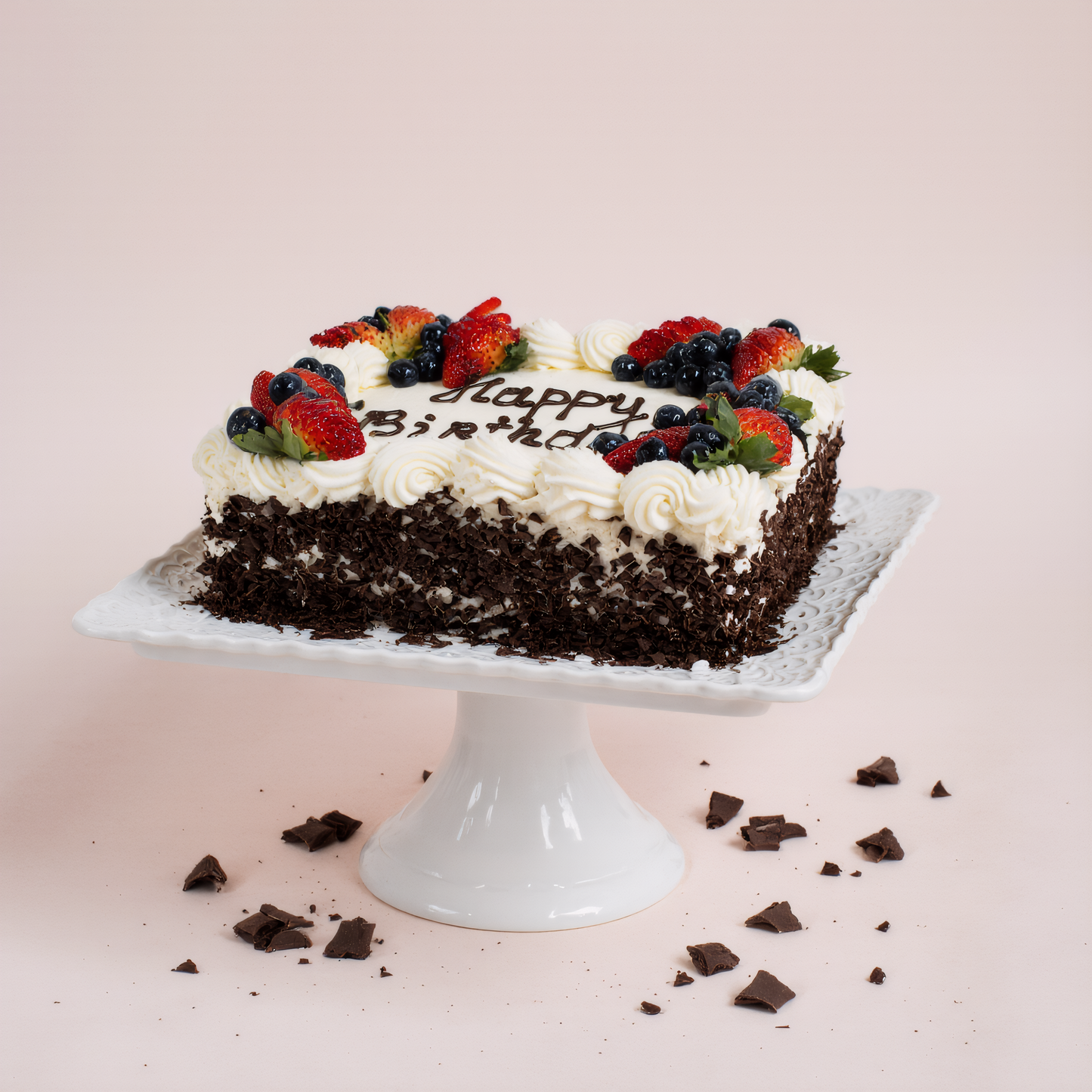Chocolate birthday cake with berries on a white stand against a light pink background