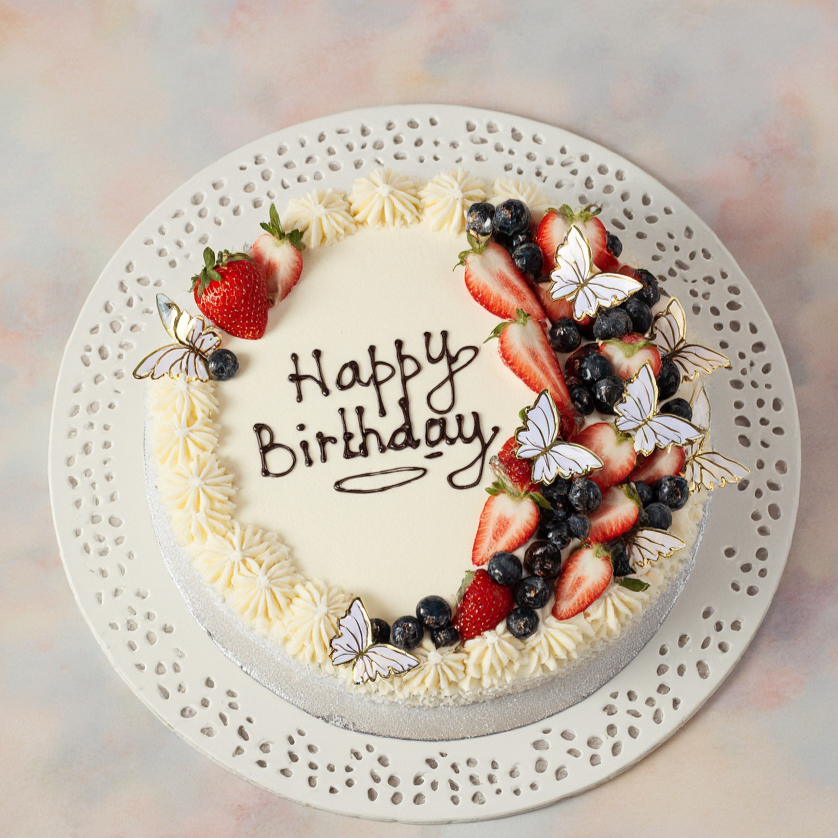 Birthday cake with strawberries, blueberries, and butterflies on a decorative plate with a pastel background.