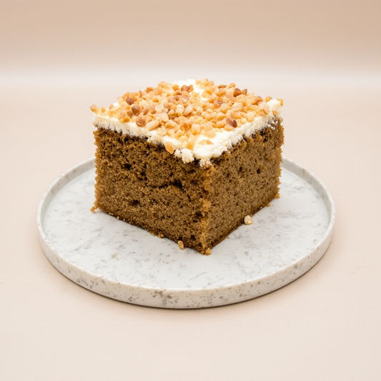 Slice of cake with white frosting and crumb topping on a speckled plate against a beige background